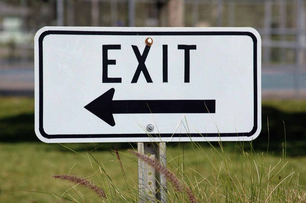 white-road-sign-with-black-letters-spelling-exit-and-an-arrow-pointing-left
