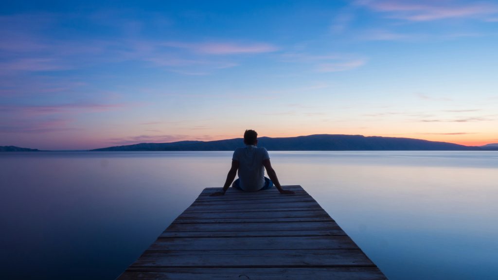 Man-sitting-on-pier-at-sunset-overlooking-water-and-contemplating