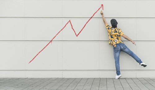 Digital composite of young man drawing a line graph at a wall